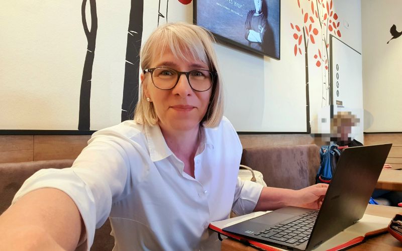 Frau sitzt an Laptop und macht ein Selfie