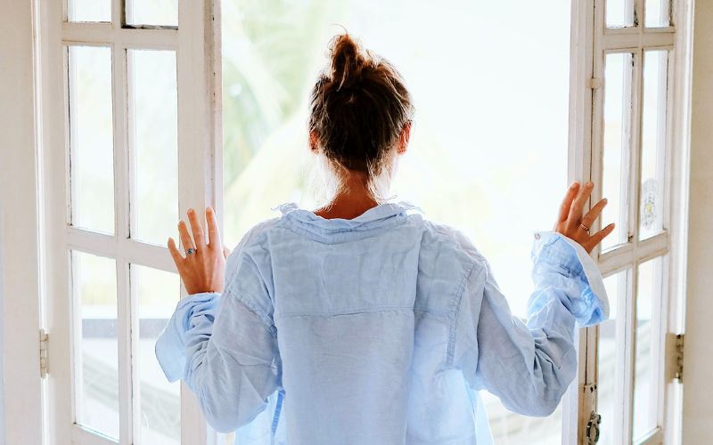 Frau in hellblauem Hemd steht am Fenster