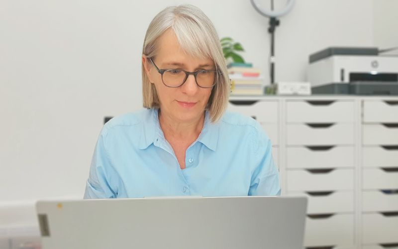 Blonde Frau mit Brille sitzt schreibend am Laptop